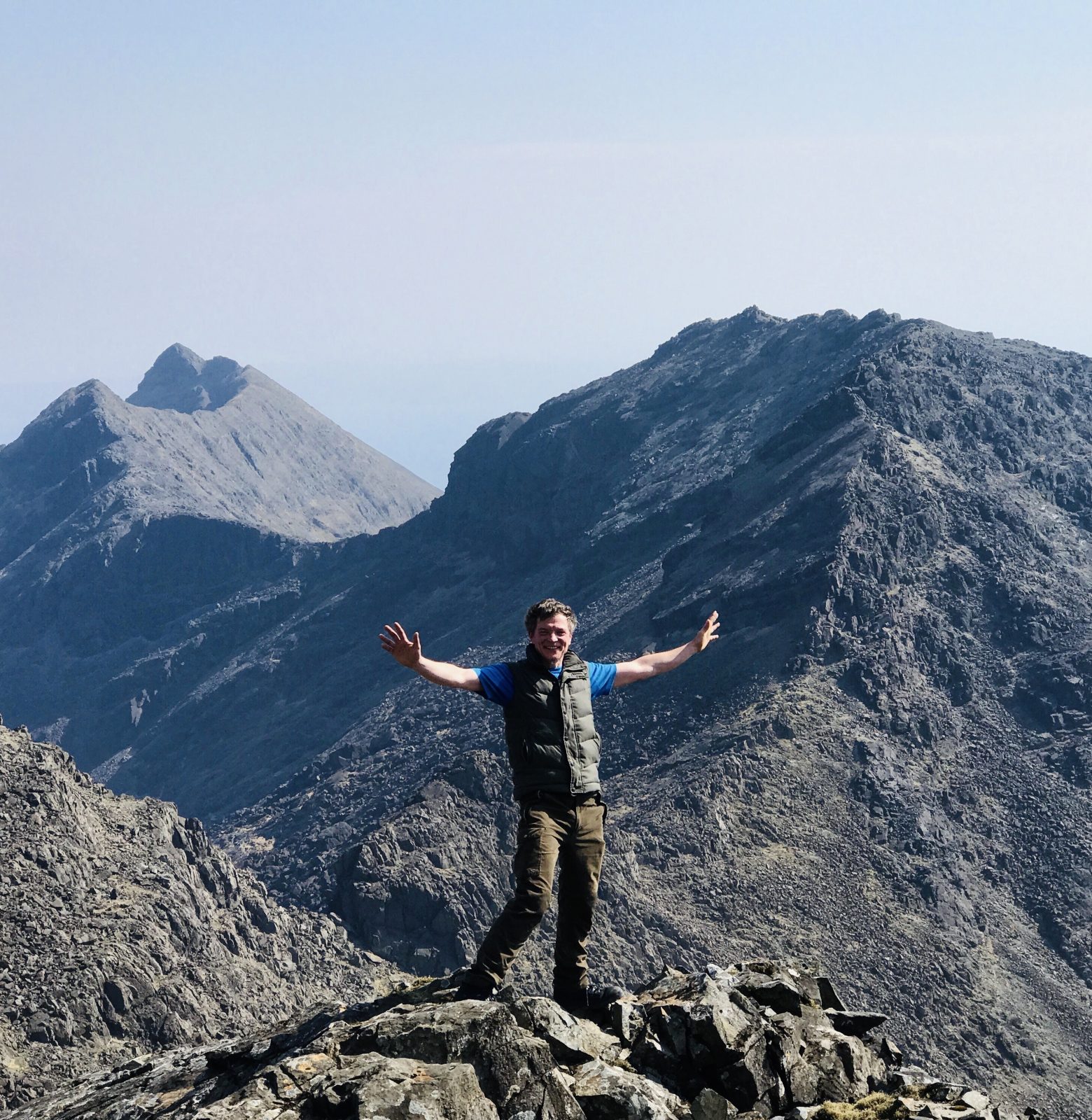 A man with outstretched arms like a bird's wings standing on summit of rocky mountain with clear blue sky